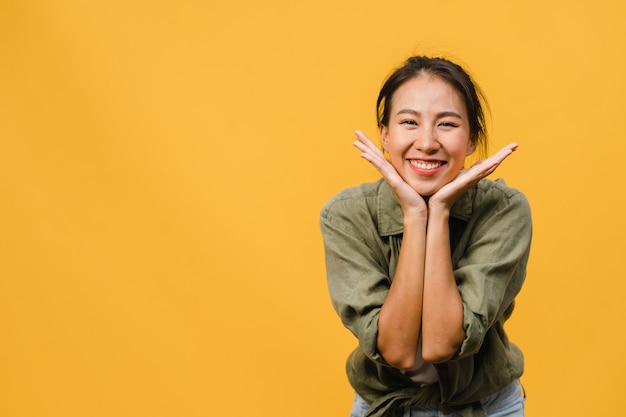 Jonge Aziatische dame met positieve uitdrukking, breed glimlachen, gekleed in casual kleding over gele muur. Gelukkige schattige blije vrouw verheugt zich over succes. Gezichtsuitdrukking concept.