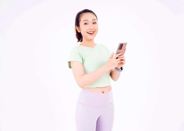 Jonge Aziatische dame toont leeg smartphonescherm met positieve uitdrukking glimlacht breed gekleed in casual kleding, voelt zich gelukkig op blauwe achtergrond Mobiele telefoon met wit scherm in vrouwelijke hand