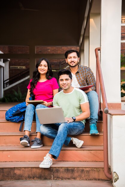 Jonge Aziatische Indiase studenten die boeken lezen, op laptop studeren, zich voorbereiden op een examen of aan een groepsproject werken terwijl ze op gras, trap of trappen van de universiteitscampus zitten