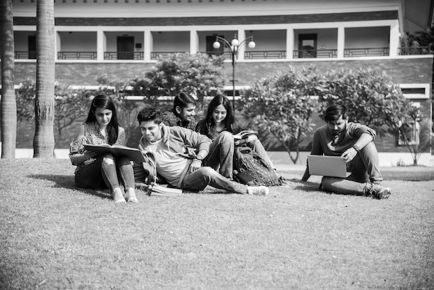 Jonge Aziatische Indiase studenten die boeken lezen, op laptop studeren, zich voorbereiden op een examen of aan een groepsproject werken terwijl ze op gras, trap of trappen van de universiteitscampus zitten