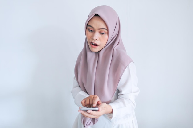 Jonge Aziatische islamvrouw die een hoofddoek draagt, is geschokt en wauw in de Indonesische vrouw op een grijze achtergrond