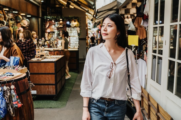 Jonge aziatische japanse vrouw toerist loopt langs kraampjes en stands van de chinese markt op zonnige dag. charmante vrouwelijke winkels in een populair gebied. gelukkig lachend jong meisje reiziger ontspannen door verkoper buiten