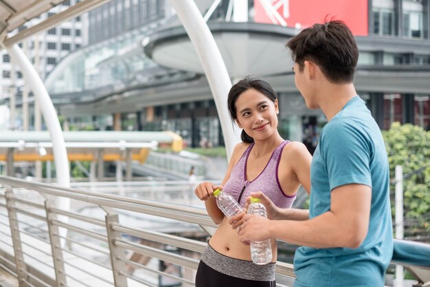 Jonge aziatische koppelatleten die rusten met een waterfles na het sporten op de brug in de stad