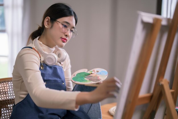 Jonge Aziatische kunstenaar gebruikt penseel en kleur om te tekenen en schilderen en creëert kunstwerken op doek