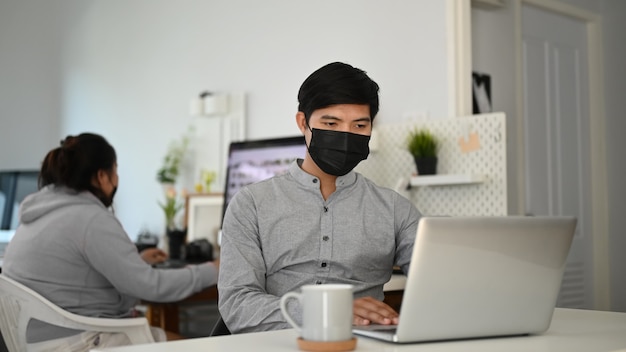 Jonge Aziatische man aan het werk op een laptop aan zijn bureau