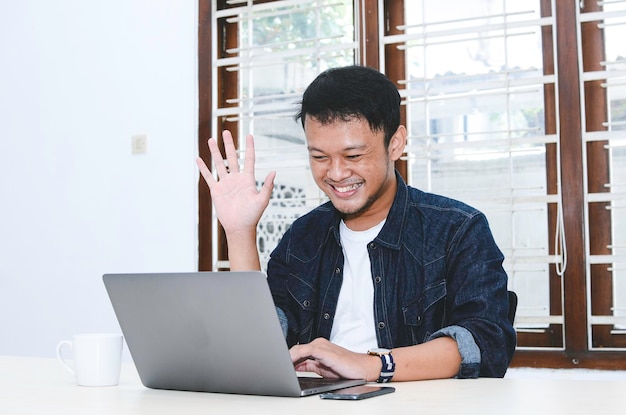 Jonge Aziatische man blij en opgewonden wanneer videogesprek met laptop op tafel