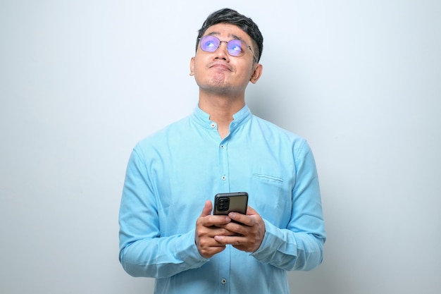 Jonge Aziatische man die een mobiele telefoon gebruikt die denkt en een half lichaamsportret opzoekt
