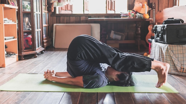 Jonge Aziatische man die yoga beoefent in een houten kamer die in pose zit Plow Pose gezond leven concept