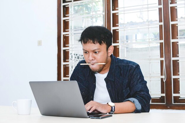 Jonge Aziatische man die zich serieus voelt als een laptop op tafel werkt