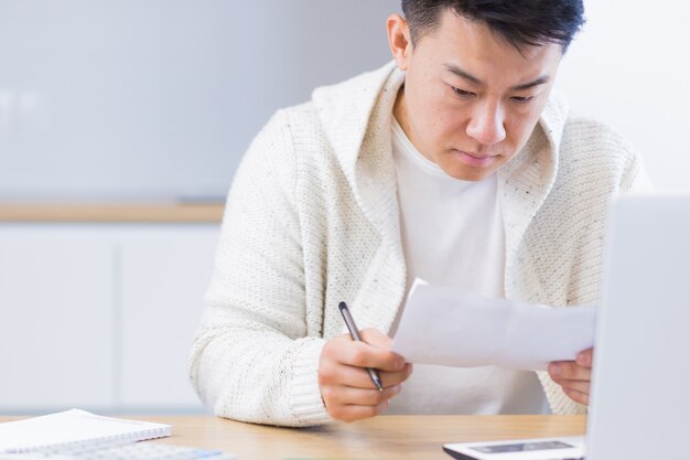 jonge Aziatische man doet papierwerk thuis zittend aan een bureau