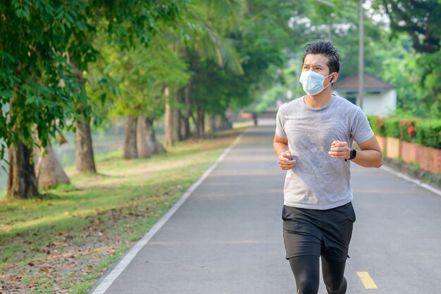 Jonge Aziatische man Draag een fitnessmasker Hardlopen in het park Zweten van een ochtendtrainingconcept: draag een masker tegen SARS-Cov-2.