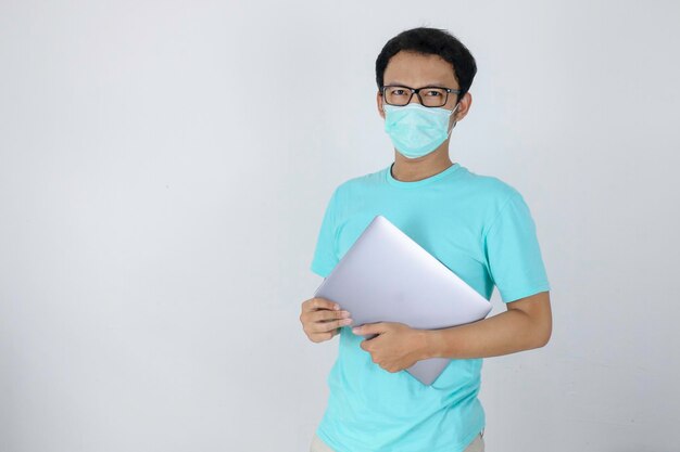 Jonge Aziatische man draagt medisch masker draagt een laptop Indonesische man met blauw shirt