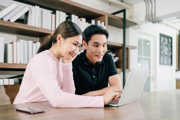 Jonge Aziatische man en vrouw met een roze trui die met een glimlach samen aan een laptop werkt