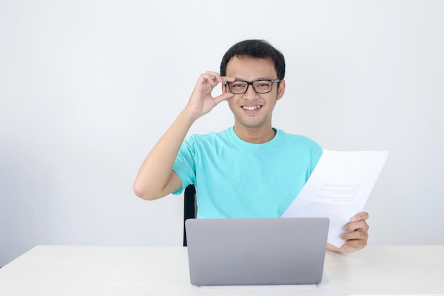 Jonge Aziatische man glimlacht en gelukkig wanneer hij op een laptop werkt en documenteert Indonesische man met blauw shirt