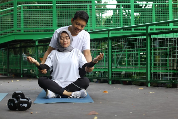 Jonge Aziatische man helpt zijn vrouw meditatie te doen in het park. Gezonde levensstijl paar concept.