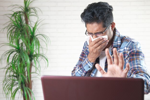 jonge Aziatische man hoesten en niest bezig met laptop
