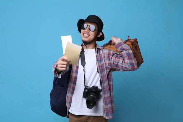 Foto jonge aziatische man in brillen met een positieve glimlach reist naar het buitenland, met kaartjes en tas