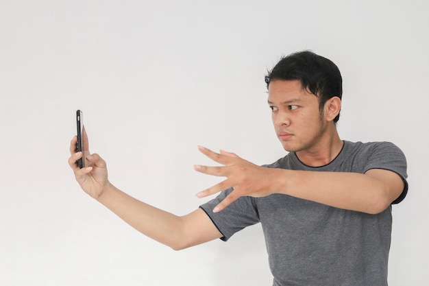 Jonge Aziatische man in grijs t-shirt Ernstig voelen en focussen met het vasthouden van de telefoon en een magisch handgebaar