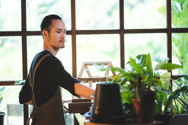 Jonge Aziatische man is blij met het kweken van planten in een kleine groene tuin thuis, hobbylevensstijl met groene natuur in een huis, bloemboom in pot tot botanische tuinbouw landbouwteelt