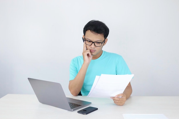 Jonge Aziatische man is serieus en concentreert zich bij het werken op een laptop en documenteert op tafel Indonesische man met blauw shirt