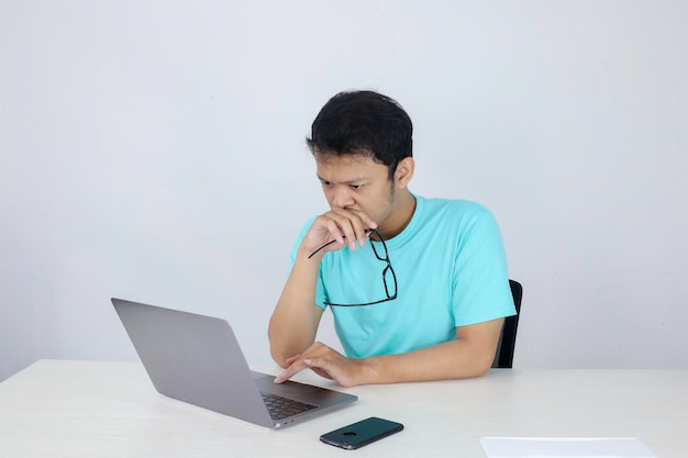 Jonge Aziatische man is serieus en concentreert zich bij het werken op een laptop op de tafel Indonesische man met een blauw shirt