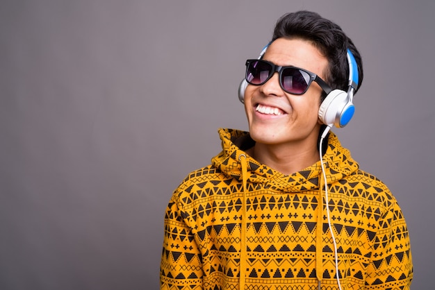 jonge Aziatische man luisteren naar muziek terwijl het dragen van hoodie tegen grijze muur