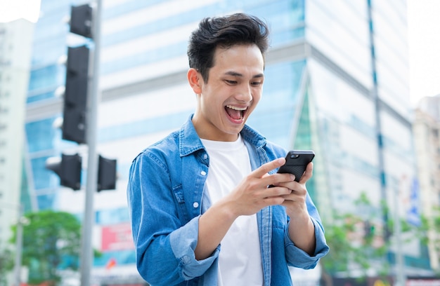 Jonge Aziatische man met behulp van smartphone tijdens het wandelen op straat