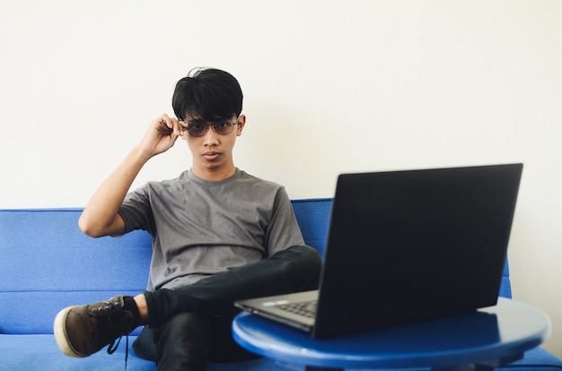 Jonge Aziatische man met een ash-shirt voor de laptop die op de bank zit