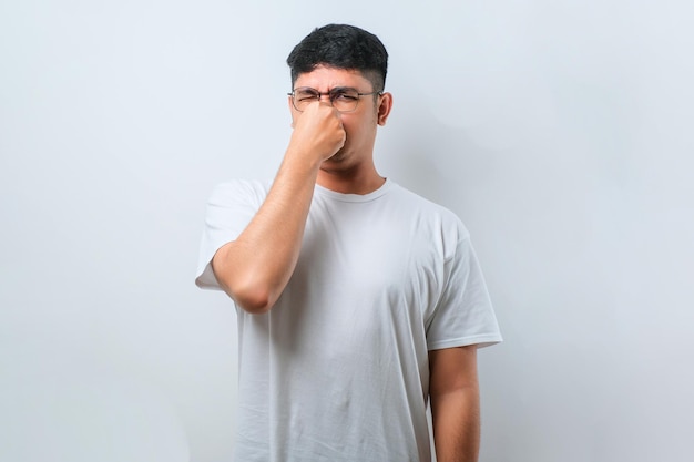 Jonge aziatische man met een casual shirt dat iets stinkt en een walgelijke, ondraaglijke geur ruikt die de adem inhoudt met vingers op de neus