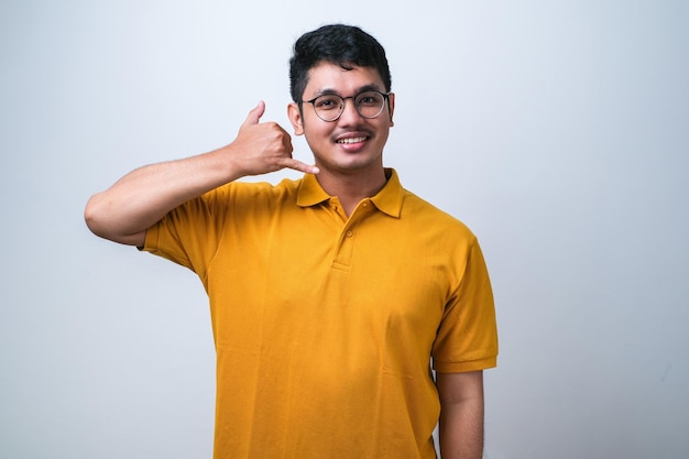 Jonge aziatische man met een casual shirt over een witte achtergrond die lacht en een telefoongebaar doet met de hand en vingers, zoals praten aan de telefoon. Communiceren van concepten