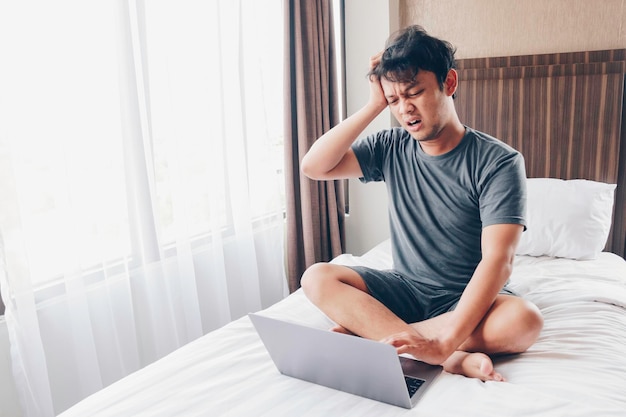 Jonge aziatische man met een laptop in bed is verward en stress Werk vanuit huis concept