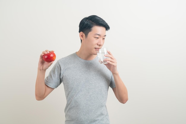 jonge Aziatische man met glas water en appel bij de hand - gezond concept