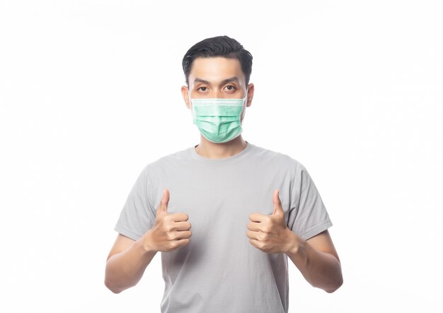 Jonge Aziatische man met hygiënisch masker en duimen opdagen om infectie, 2019-nCoV of coronavirus te voorkomen. Luchtwegaandoeningen zoals pm 2,5 vechten en griep. geïsoleerd