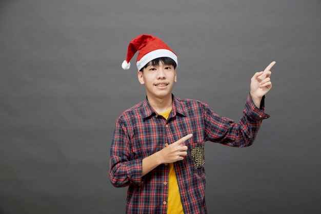 Jonge Aziatische man met kerstmuts op studio-opname, geïsoleerd op een grijze achtergrond