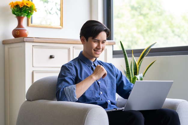 Jonge Aziatische man met laptop in de woonkamer