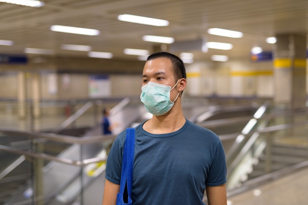 Jonge Aziatische man met masker voor bescherming tegen uitbraak van coronavirus op het metrostation