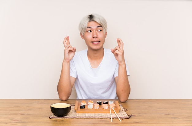 Jonge Aziatische man met sushi in een tafel met vingers kruising