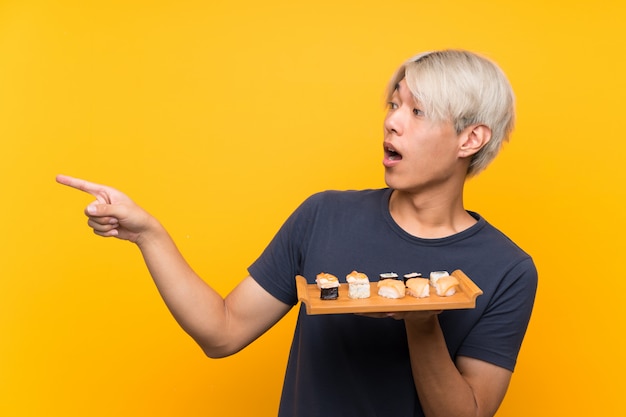 Jonge Aziatische man met sushi over geïsoleerde gele wijzende vinger aan de zijkant