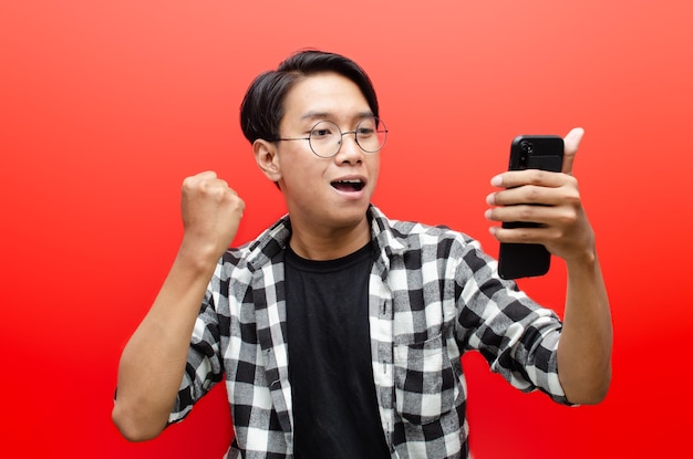 jonge Aziatische man met telefoon in verschillende uitdrukkingen verdrietig, blij, geschokt, boos geïsoleerd over rood.
