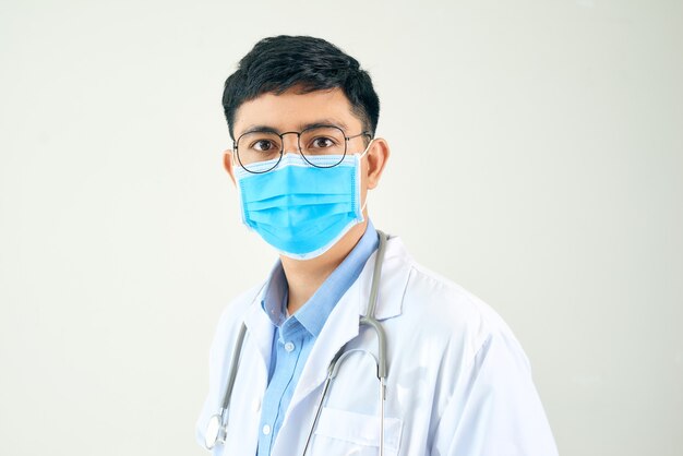 Jonge Aziatische man op medisch gebied, gekleed in een witte jas en gezichtsmasker,