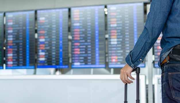 Jonge Aziatische man toeristische rugzak met gezichtsmasker met koffer op internationale luchthaven kijken naar het vluchtinformatiebord en zijn vlucht controleren Man wachten op vlucht Reisconcept