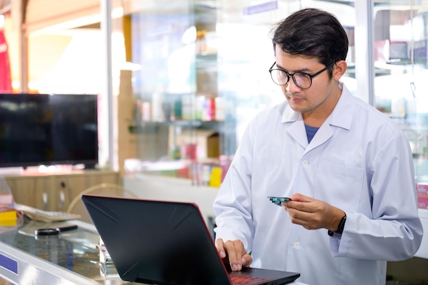 Jonge Aziatische mannelijke apotheker die medicijnen controleert in de apotheekinventaris met behulp van een computer bij een apotheek met foto's van hoge kwaliteit