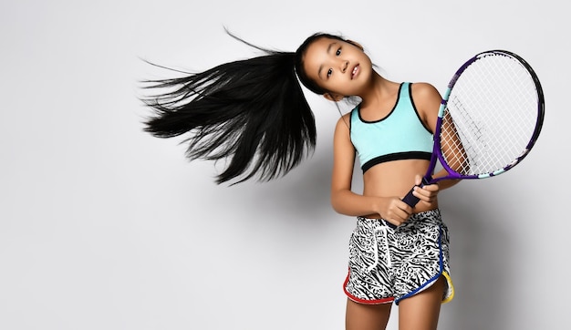 Jonge Aziatische meisje preteen grote tennisser met racket in beweging studio shot portret op kopie ruimte mooi sportief vrouwelijk kind met oosterse uitstraling en sportkleding camera kijken