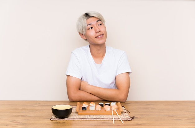Jonge Aziatische mens met sushi in een en lijst die omhoog lacht kijkt