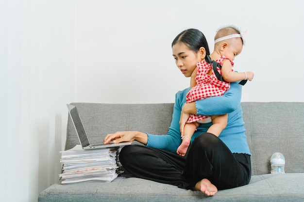 Jonge Aziatische moeder met schattige babydochter die samen op de bank in de woonkamer zit