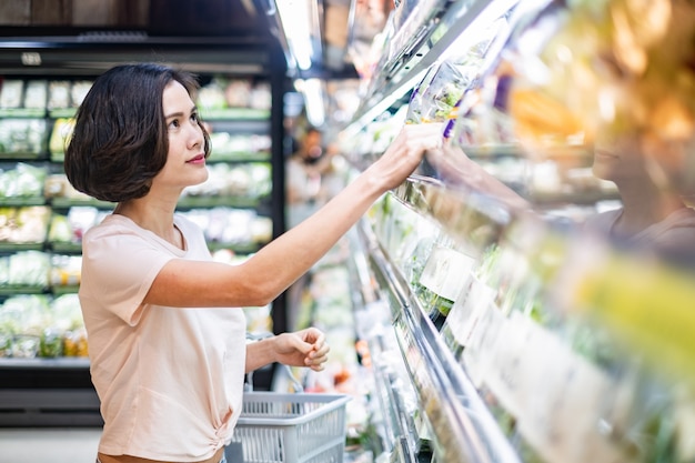 Jonge Aziatische mooie de kruidenierswinkelmand die van de vrouwenholding in supermarkt lopen.