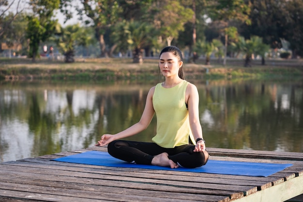 Jonge Aziatische mooie vrouw die yoga beoefent en mediteert in de lotushouding buiten naast het meer in de ochtend voor ontspanning en gemoedsrust. Harmonie en meditatie concept. Gezonde levensstijl