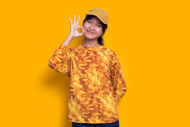Jonge Aziatische mooie vrouw met ok teken gebaar omhoog geïsoleerd op gele achtergrond