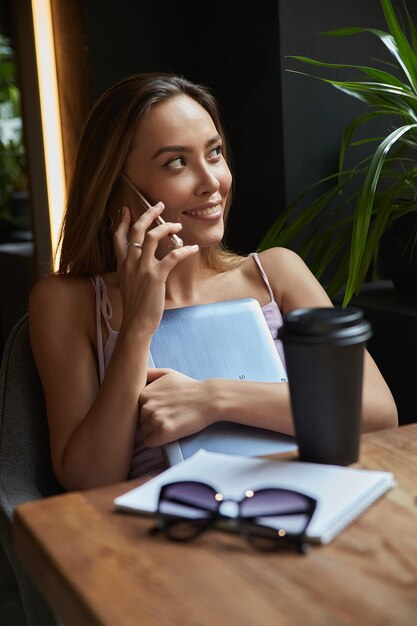 Jonge aziatische mooie vrouw zittend aan tafel van coffeeshop bellen met smartphone