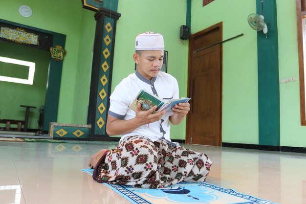 Jonge aziatische moslim die in de moskee bidt en Al Quran . leest